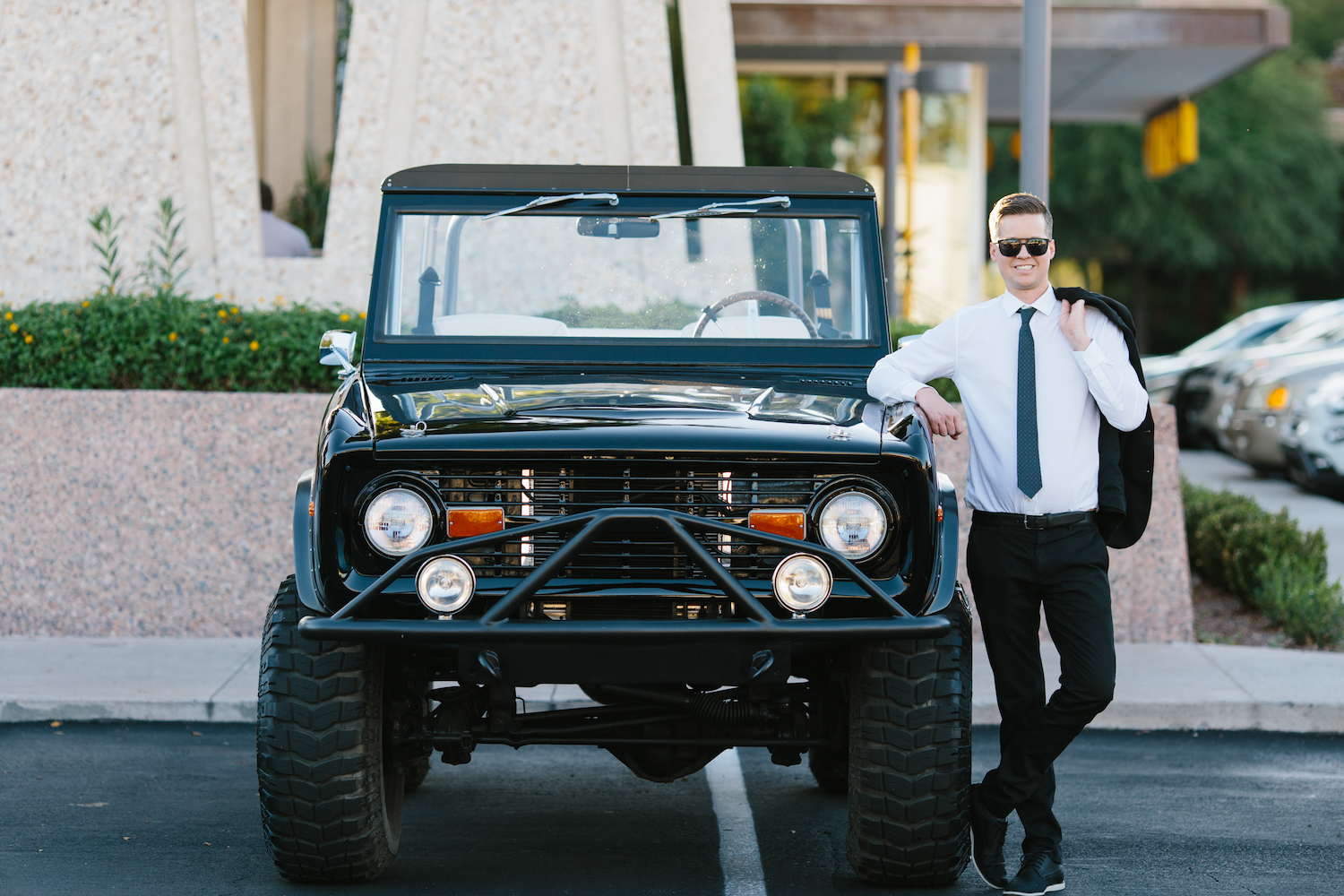 A man in a suit stands next to a black Ford Bronco